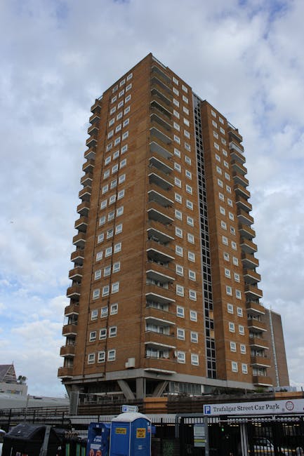 Close-up view of a high-rise residential building's exterior façade, showcasing multiple balconies with metal railings and glass doors. The balconies are constructed from grey concrete with some wood-paneled sections, and a few feature potted plants and outdoor furniture. The windows are clean and reflective, with natural light highlighting the textured surface of the building. This image emphasizes the building's structural materials and outdoor spaces, illustrating the typical exterior surfaces encountered in residential flats along Vauxhall Bridge Road. Pimlico Carpet Cleaners specializes in surface cleaning and maintenance, including deep cleaning and sanitisation of various residential façades and external surfaces in the Pimlico area.